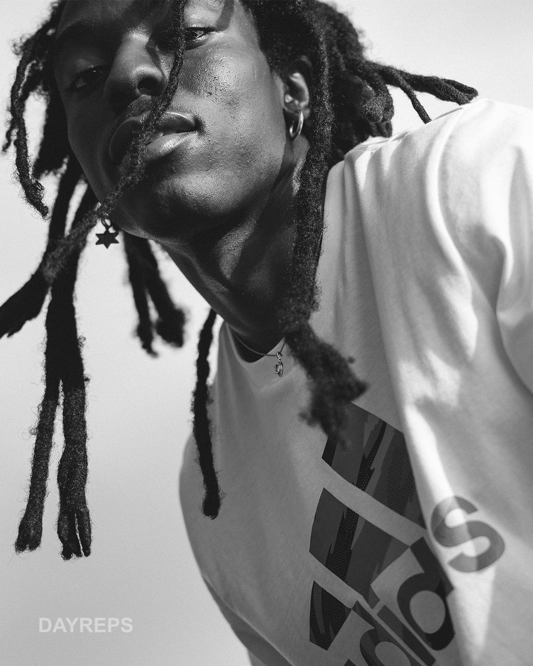 Close-up portrait of a Black man with dreadlocks wearing an Adidas t-shirt, photographed by Nick Laham.