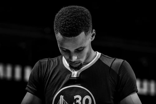 Monochrome portrait of a basketball player in his jersey with the number 30 looking down, captured with a medium shot in a studio.