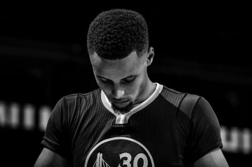 Monochrome portrait of a basketball player in his jersey with the number 30 looking down, captured with a medium shot in a studio.