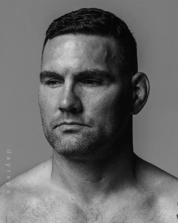 Black and white portrait of a shirtless man with short dark hair looking off to the side, photographed by Nick Laham