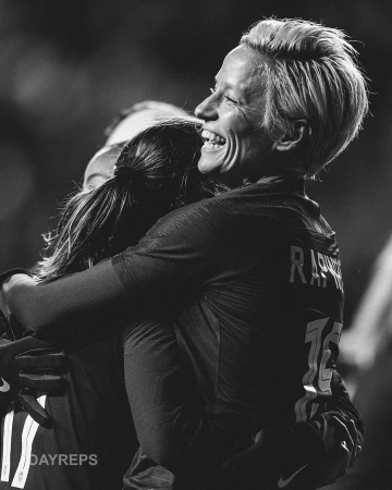 Two smiling athletes in soccer uniforms embrace on a field. The scene is black and white, capturing an emotional moment of celebration.