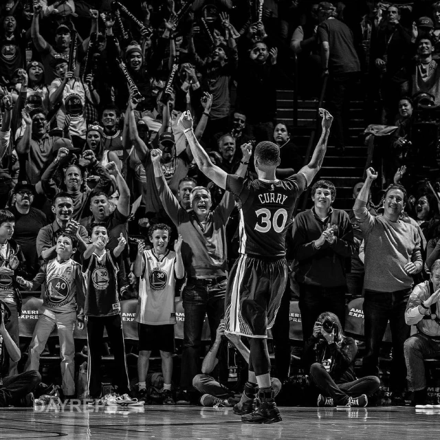 Black and white photo of Stephen Curry in action on the basketball court, celebrating a victory in front of a cheering crowd.
