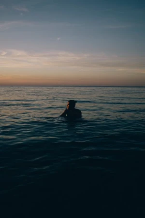 Person standing waist-deep in the calm ocean under a twilight sunset sky, captured by Nick Laham