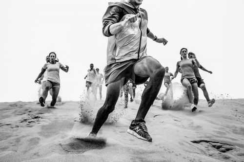 Monochrome shot of a group of runners sprinting down a sand dune with motion blur, showcasing fitness, competition, and outdoor activity.