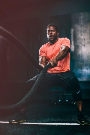 Focused adult male intensely works out with battle ropes in a fitness center, showcasing strength and determination during an exercise routine.