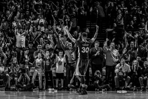 Monochrome shot of basketball player Curry #30 with arms raised, crowd cheering in stands, captured in sports event photography.