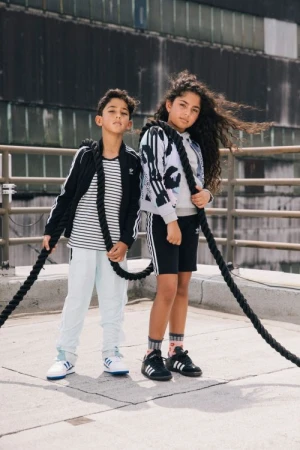 Two children holding thick black climbing ropes on a concrete rooftop by photographer Nick Laham