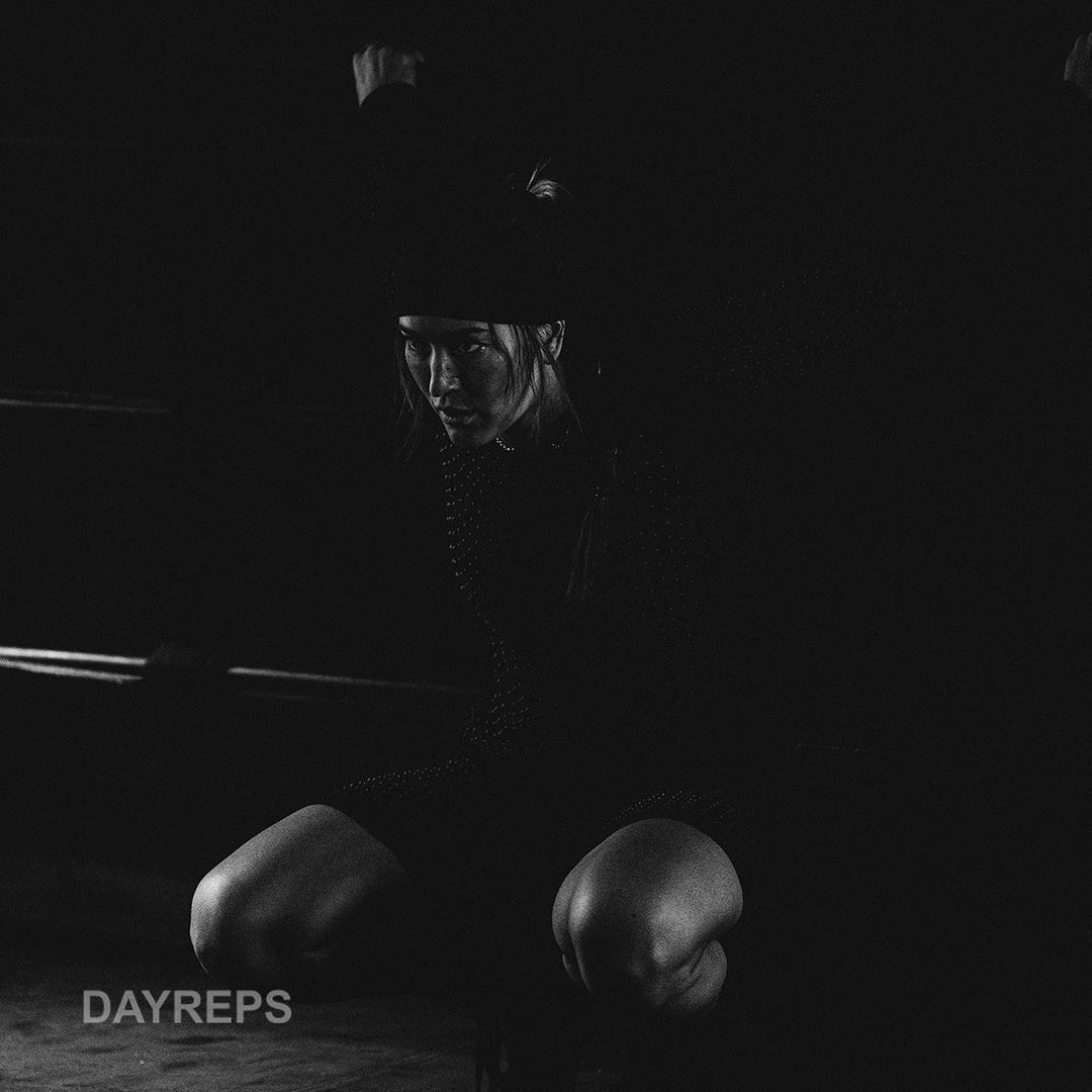 Monochromatic shot of a woman in boxing gloves crouched in a boxing ring, creating a strong contrast between light and shadow.