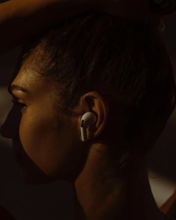 Profile shot of an adult female's face with an earbud in her ear, warm and dark lighting, and a neutral expression.