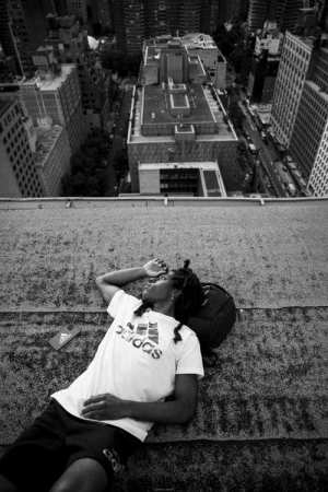 Monochrome portrait of a person lying on a high rooftop overlooking city buildings