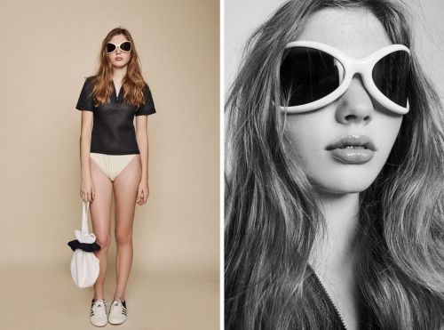 A young woman in a black top, light bottoms, sneakers, and large white sunglasses poses with a white bag against a beige background.