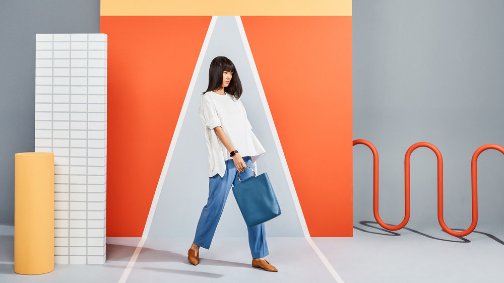 Woman in blue pants walks with a handbag against colorful geometric backdrop in a studio; fashion, style, and creative photography.
