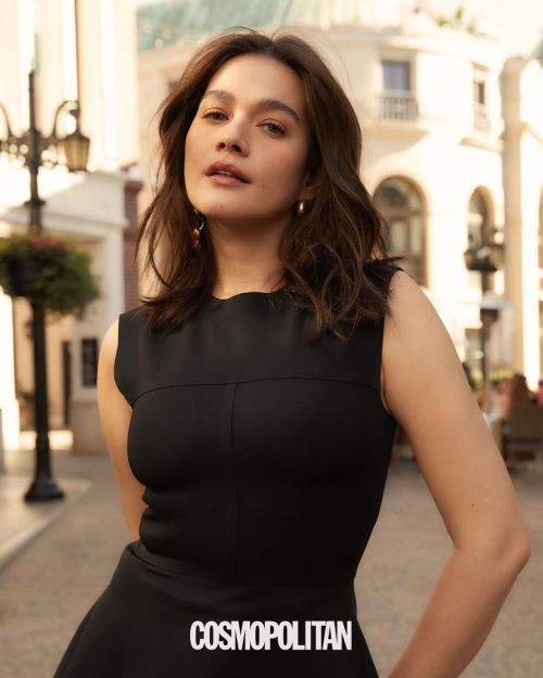 Cosmopolitan fashion shot featuring an adult woman in a black dress, medium shot, posing outdoors on a city street.