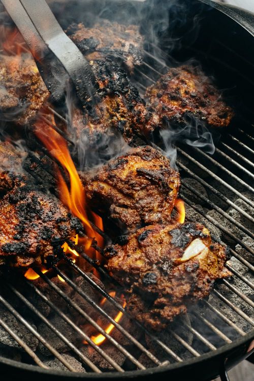 Grilled hamburgers cooking on a charcoal grill with flames licking the patties and wisps of smoke rising, shot at eye-level.