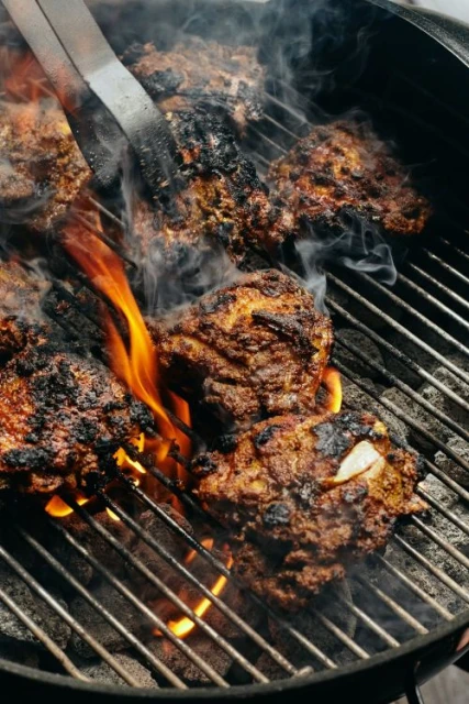 Grilled hamburgers cooking on a charcoal grill with flames licking the patties and wisps of smoke rising, shot at eye-level.