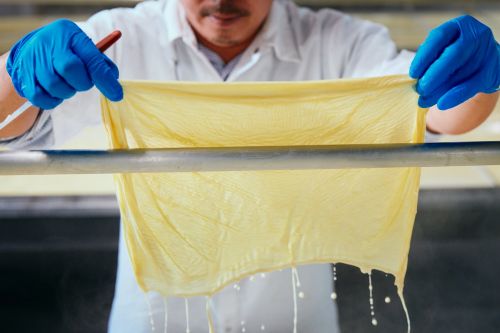 Tofu skin production shown with a worker in blue gloves and a white coat holding a yellow tofu skin and a brown stick in a factory setting.