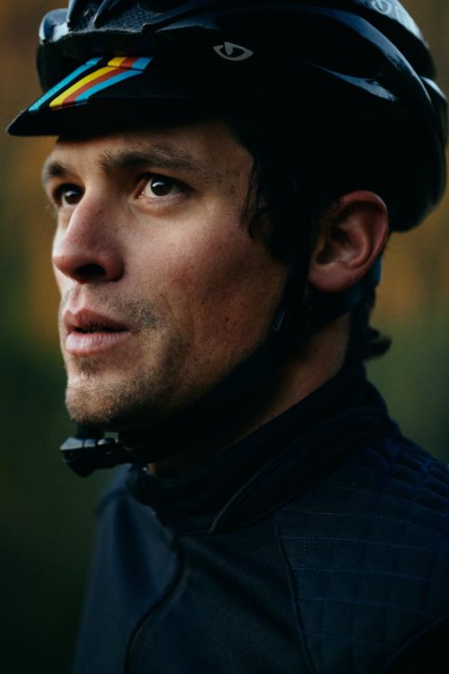 Close-up portrait of a man in a cycling helmet, looking off to the side with soft natural light illuminating his face and upper body.