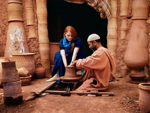 Woman and man work at a pottery wheel indoors surrounded by earthenware vessels, showcasing the creation of ceramics in a rustic setting.