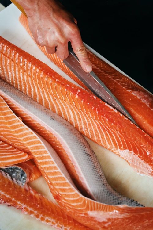 Salmon fillet being sliced with a knife on a cutting board. The scene highlights food preparation, featuring the fresh fish and culinary tools.