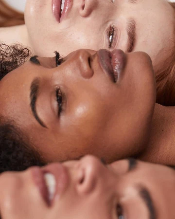 Close-up beauty portrait of three women with diverse skin tones positioned closely together