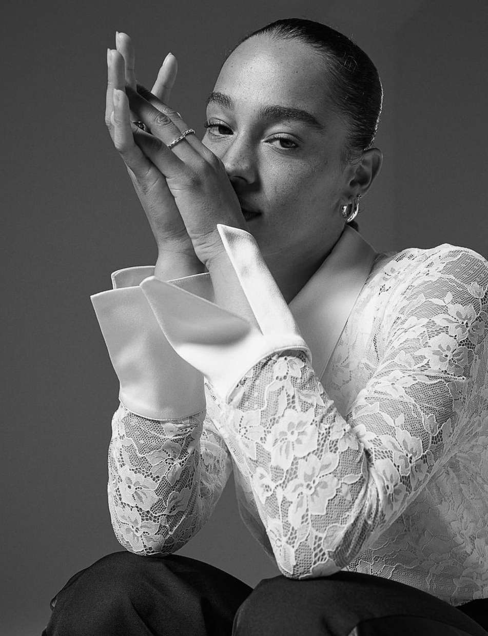 Monochrome portrait of a woman with hands raised near her face wearing a lace long-sleeve top by photographer Ali Mitton.