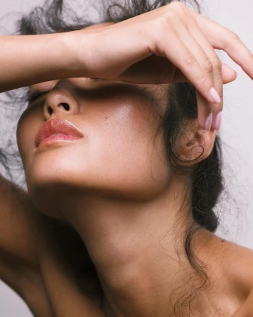 Close-up portrait of a woman with hand raised shielding her eyes against a neutral background by photographer Ali Mitton.