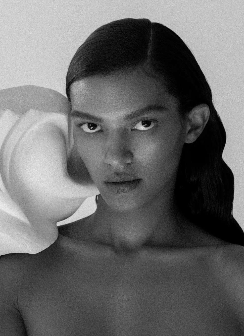 Monochrome portrait of a woman with dark hair and striking gaze, featuring a large white flower accent for beauty and fashion.