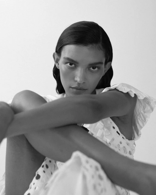 Black and white portrait of a woman with wet hair in a white, eyelet dress, posing against a neutral background in a studio.