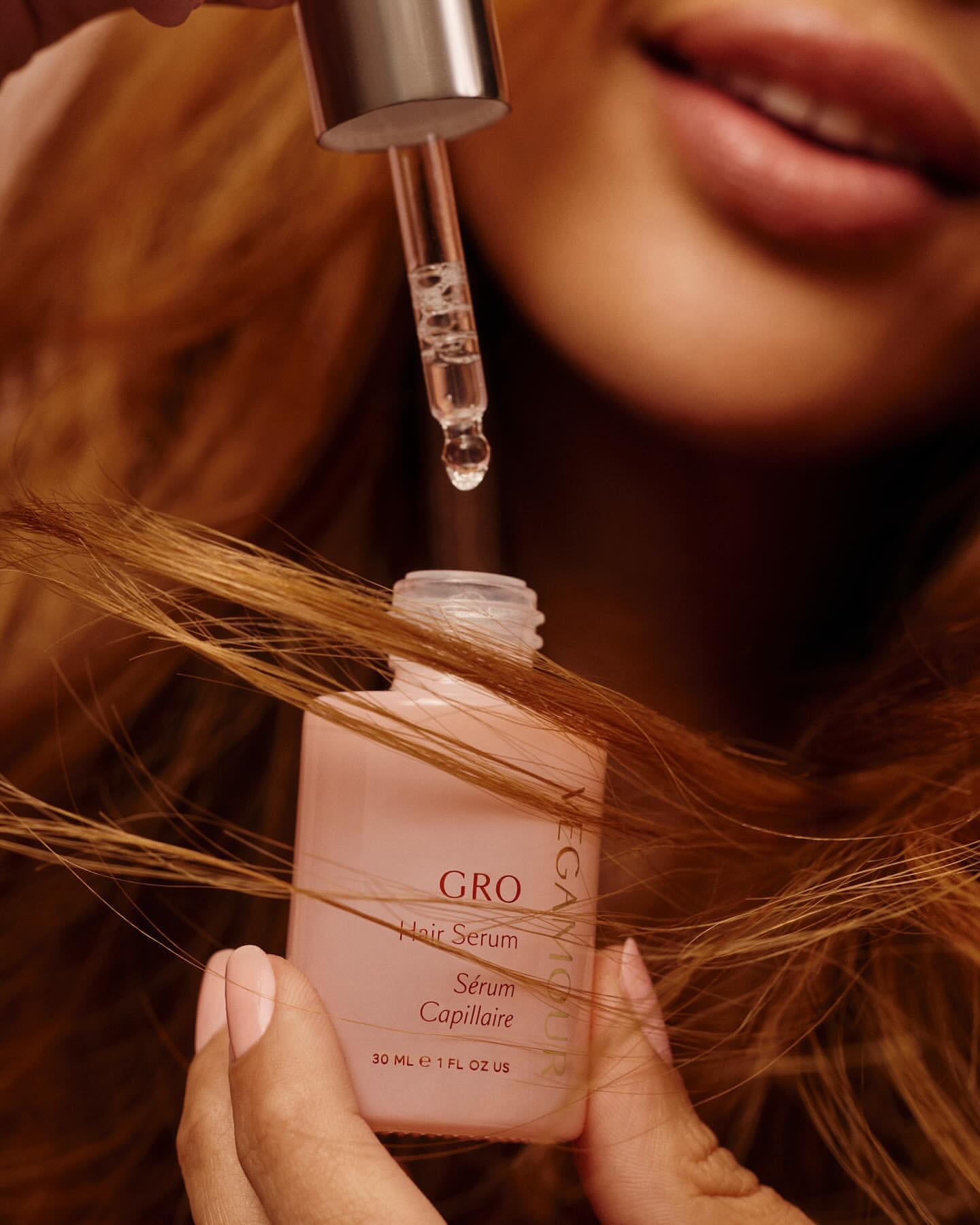 Close-up studio shot of woman holding Gro Hair Serum bottle with dropper, showcasing beauty and haircare product application.