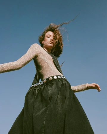 Low angle portrait of a woman in a metallic mesh top and dark denim skirt against a clear blue sky