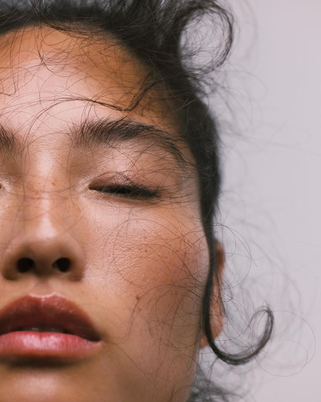 Close-up portrait of a woman with loose hair strands across her face, captured by photographer Ali Mitton.