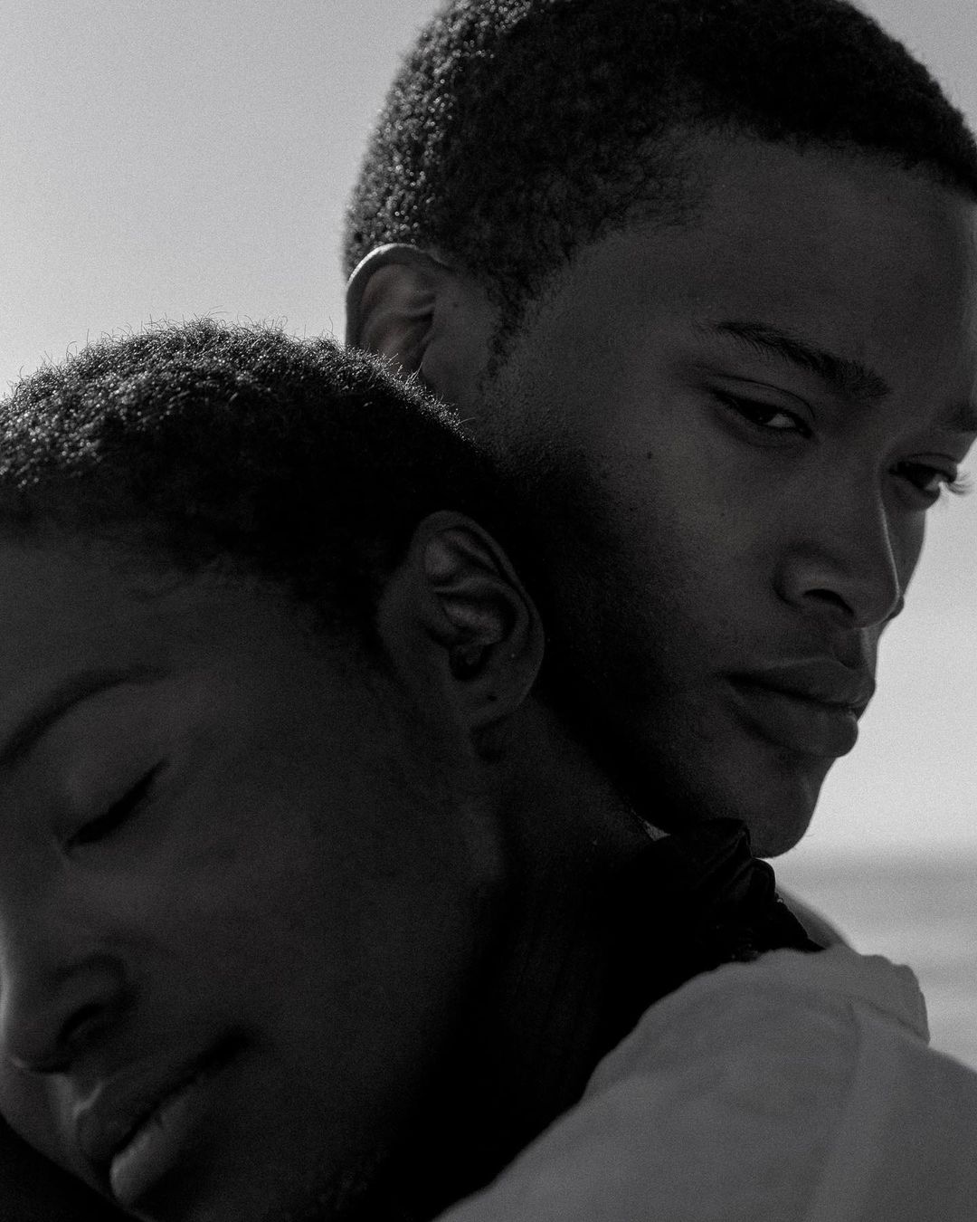 Black and white close portrait of a man and a woman embracing affectionately against a bright sky.