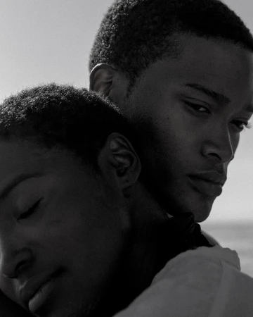 Black and white close portrait of a man and a woman embracing affectionately against a bright sky.