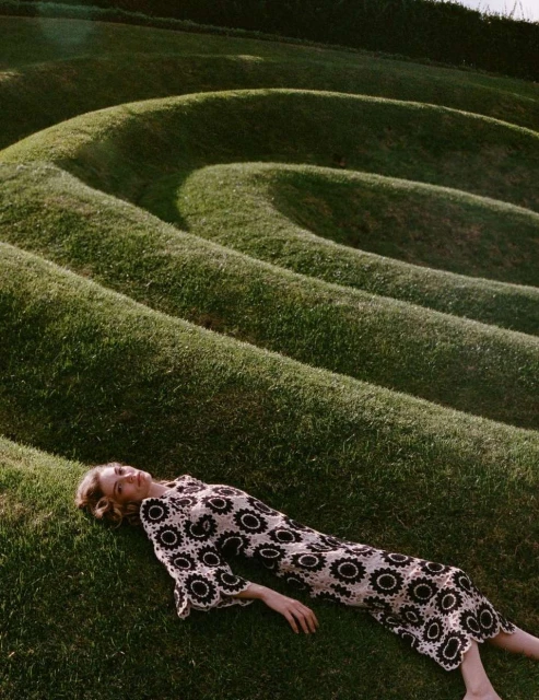 Woman in a crochet dress lying on a grass-covered, terraced landscape, creating a visually appealing and natural composition.