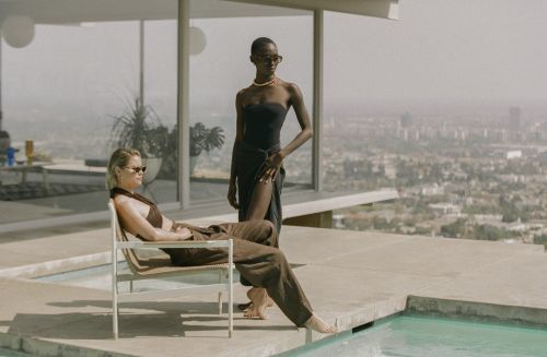 Two models posing by a pool overlooking a city skyline, photographed by Ali Mitton.