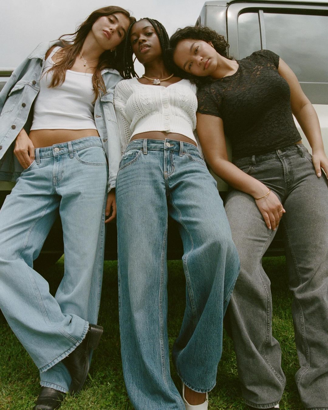 Three women in jeans and casual tops pose together against a neutral backdrop. The composition highlights fashion and style elements.