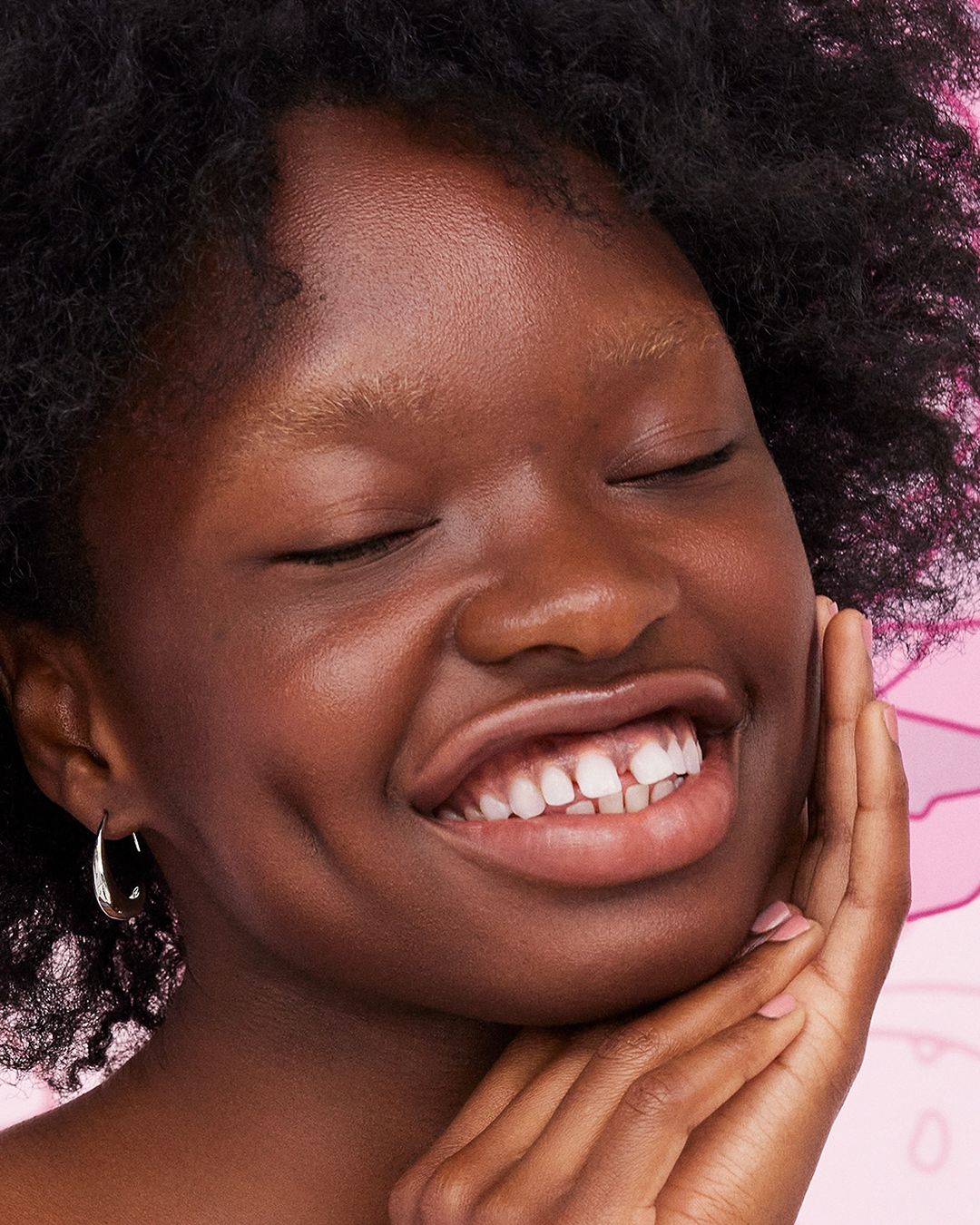 Close-up of a smiling African-American woman with her eyes closed, showing her face, hairstyle, gold hoop earring, and smooth skin.