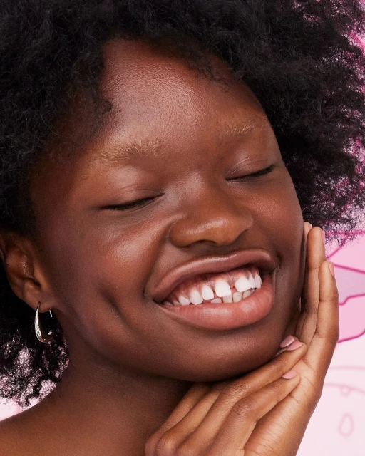Close-up of a smiling African-American woman with her eyes closed, showing her face, hairstyle, gold hoop earring, and smooth skin.