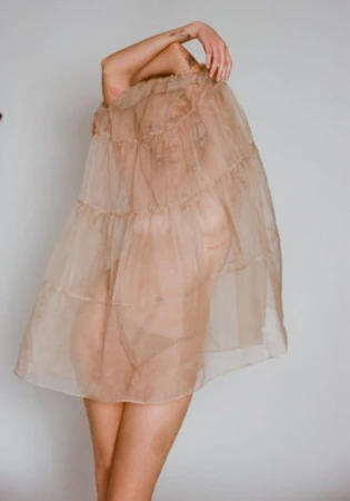 Woman posing inside a translucent beige skirt held up to cover her head and face against a white background by Ali Mitton