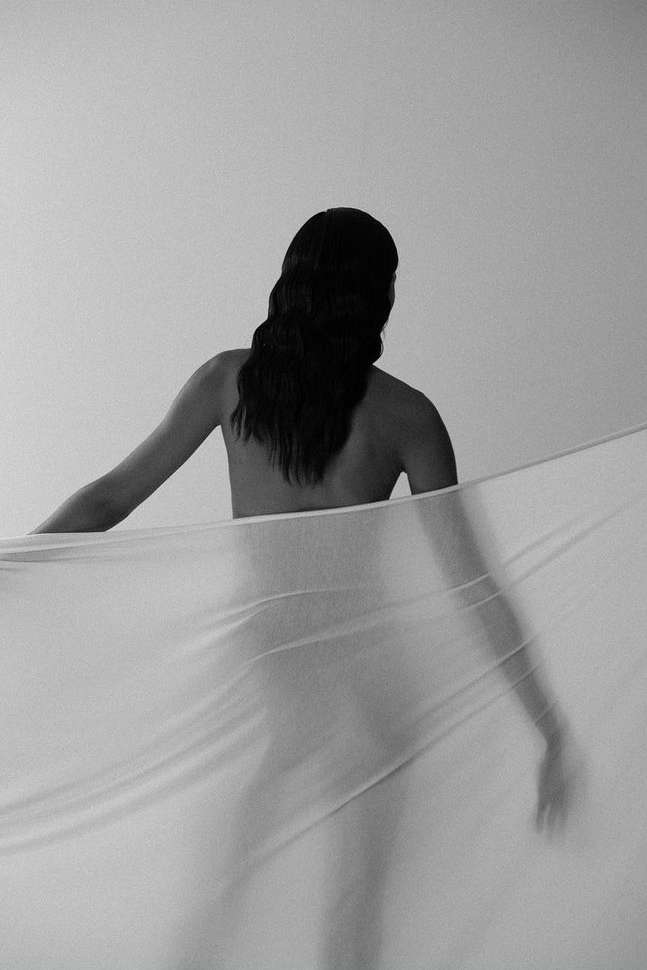 Monochrome portrait of a woman seen from behind holding a sheer white fabric banner by photographer Ali Mitton.