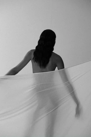 Monochrome portrait of a woman seen from behind holding a sheer white fabric banner by photographer Ali Mitton.