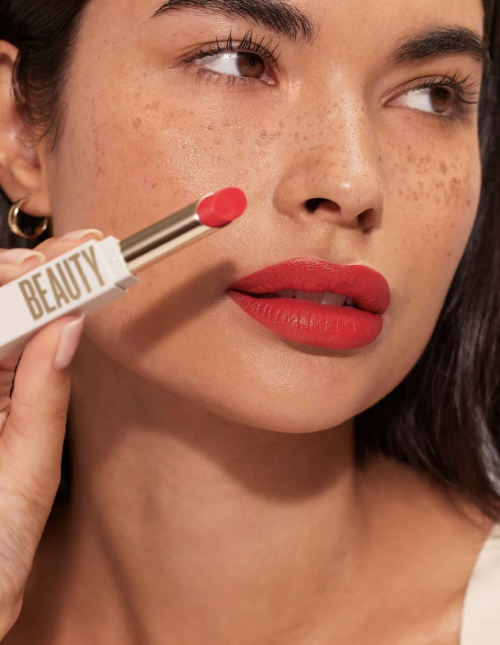 Close-up beauty portrait of a woman wearing bright red lipstick and holding a white lipstick tube near her face