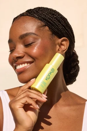 Black woman with braided hair smiling and holding a yellow skincare bottle by photographer Ali Mitton
