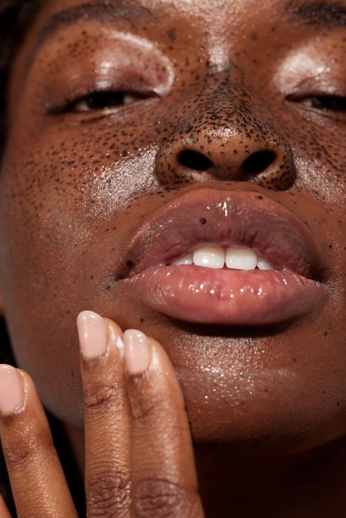 Close-up of a young Black woman's face with a radiant complexion and dewy lips, hand gently touching her cheek, beauty, skincare.