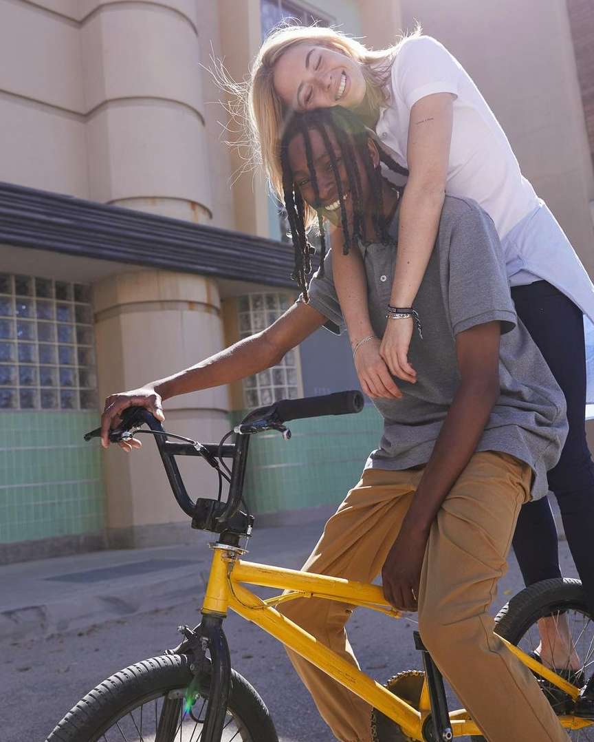 Two people, an adult male and an adult female, are outside with a yellow bicycle near a building with fair lighting conditions.