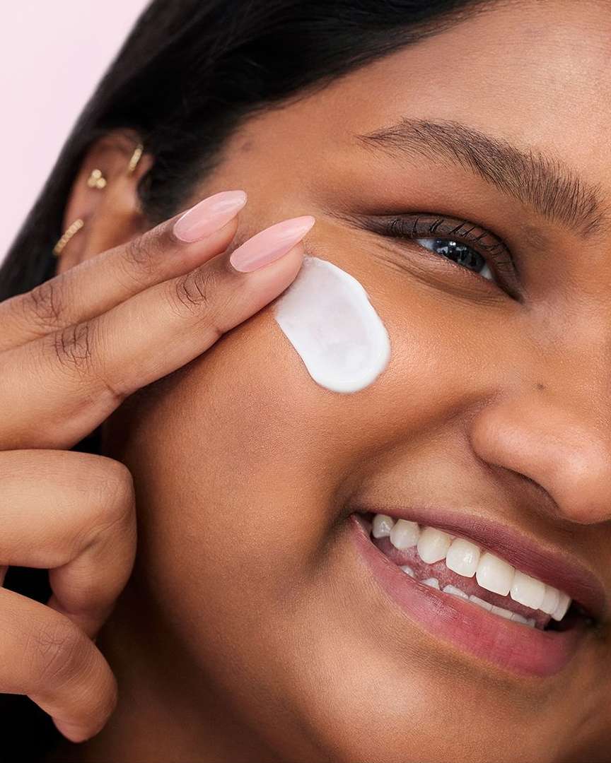 Close-up of a dark-skinned woman applying white cream to her face with her finger, showcasing skincare and beauty routine.