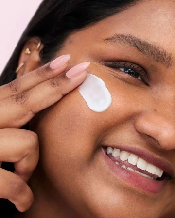 Close-up of a dark-skinned woman applying white cream to her face with her finger, showcasing skincare and beauty routine.