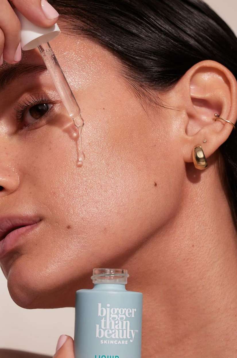 Close-up of a woman's face as she applies skincare serum with a dropper, showcasing beauty and wellness in a studio setting.