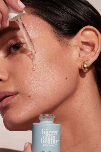 Close-up of a woman's face as she applies skincare serum with a dropper, showcasing beauty and wellness in a studio setting.