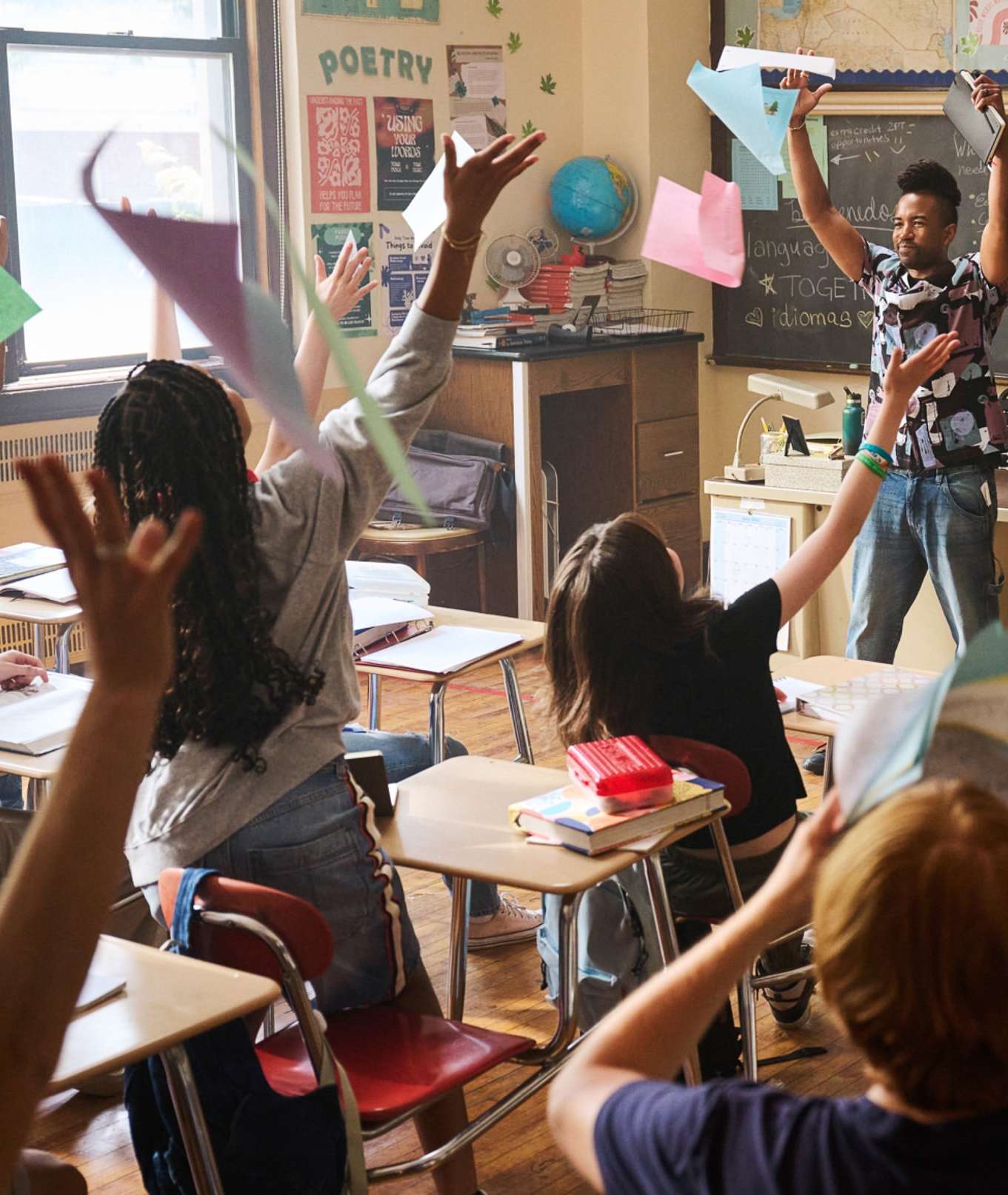 Enthusiastic teacher and students celebrate together in classroom, throwing papers in the air, capturing a lively educational moment.
